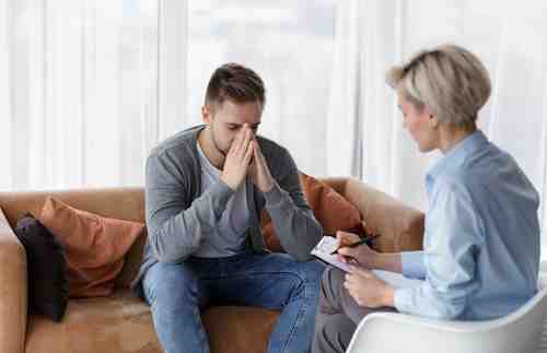 A professional alcohol recovery specialist actively listening and taking notes during a private counseling session with a client.