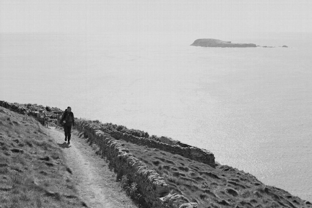 A black and white photo of a person hiking along a coastal trail, representing the mindfulness and healthy hobbies that build sober living skills.